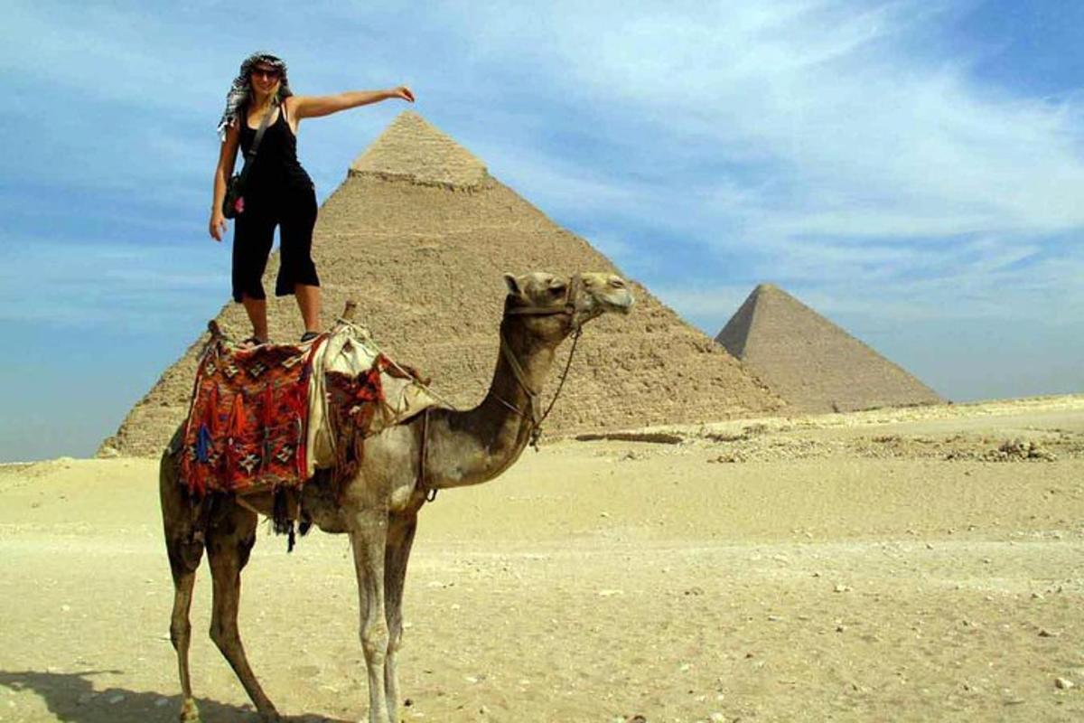 una donna in piedi su un cammello davanti alle piramidi