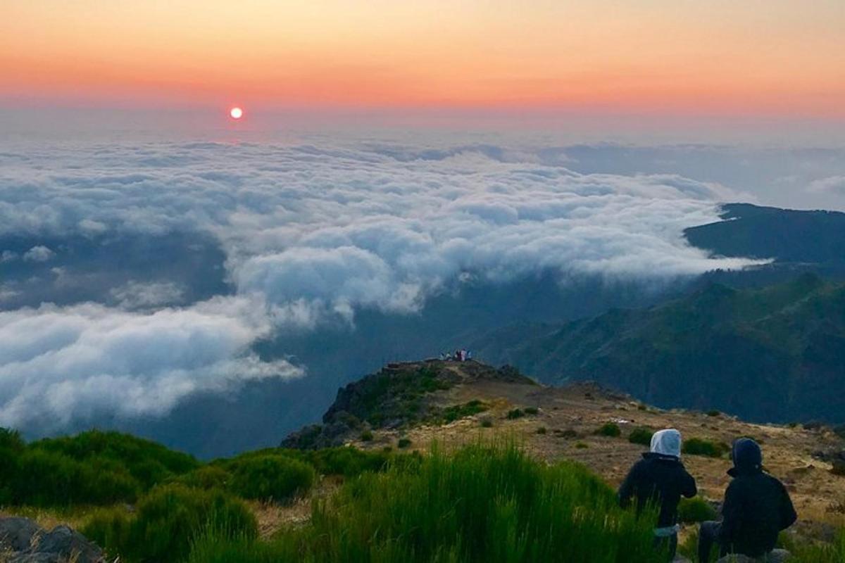 zwei Personen sitzen auf einem Berg und beobachten den Sonnenuntergang