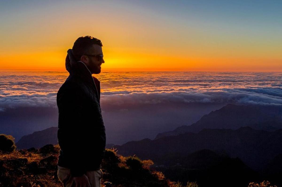 Ein Mann steht bei Sonnenuntergang auf einem Berggipfel