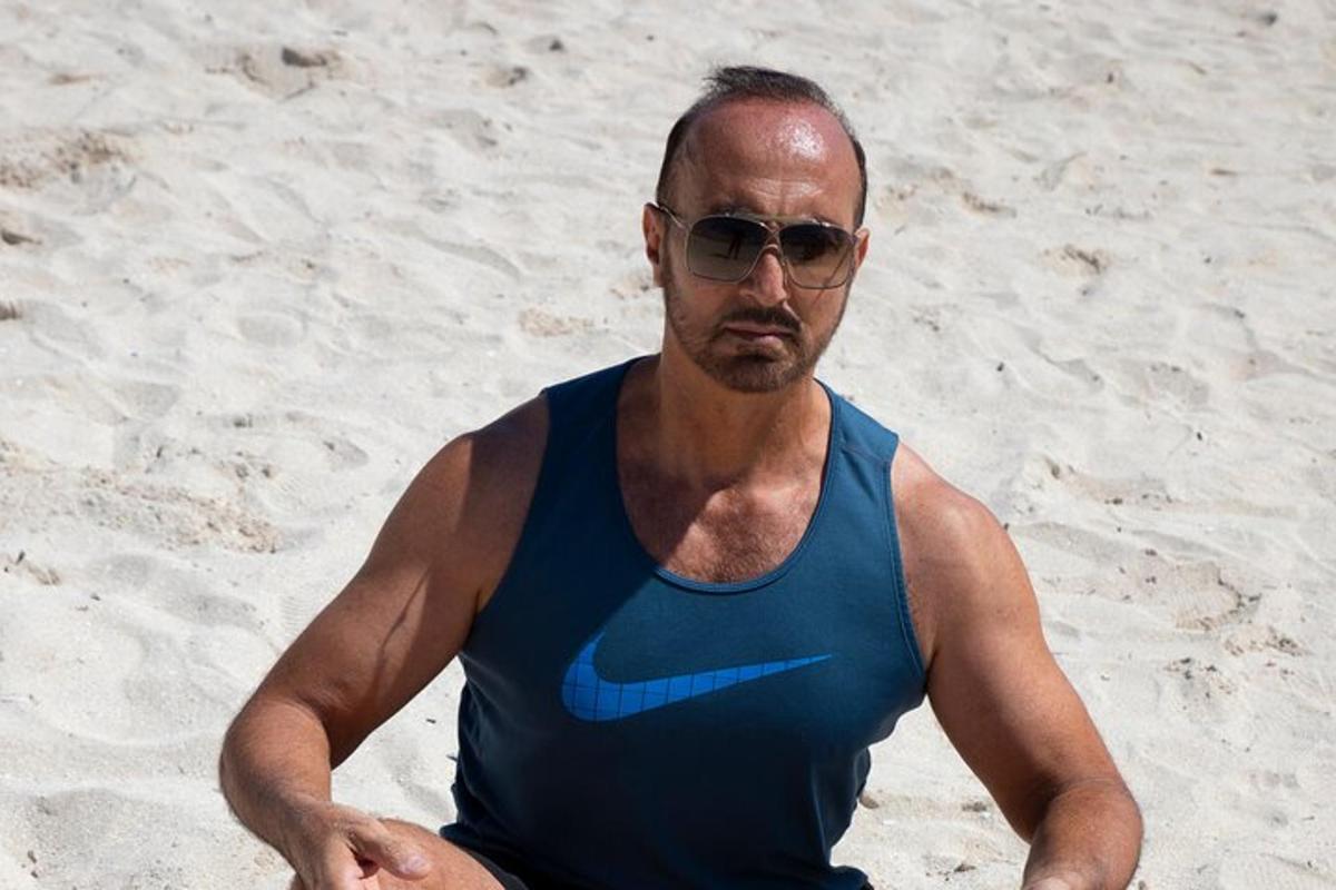 a man in a blue tank top sitting on the beach