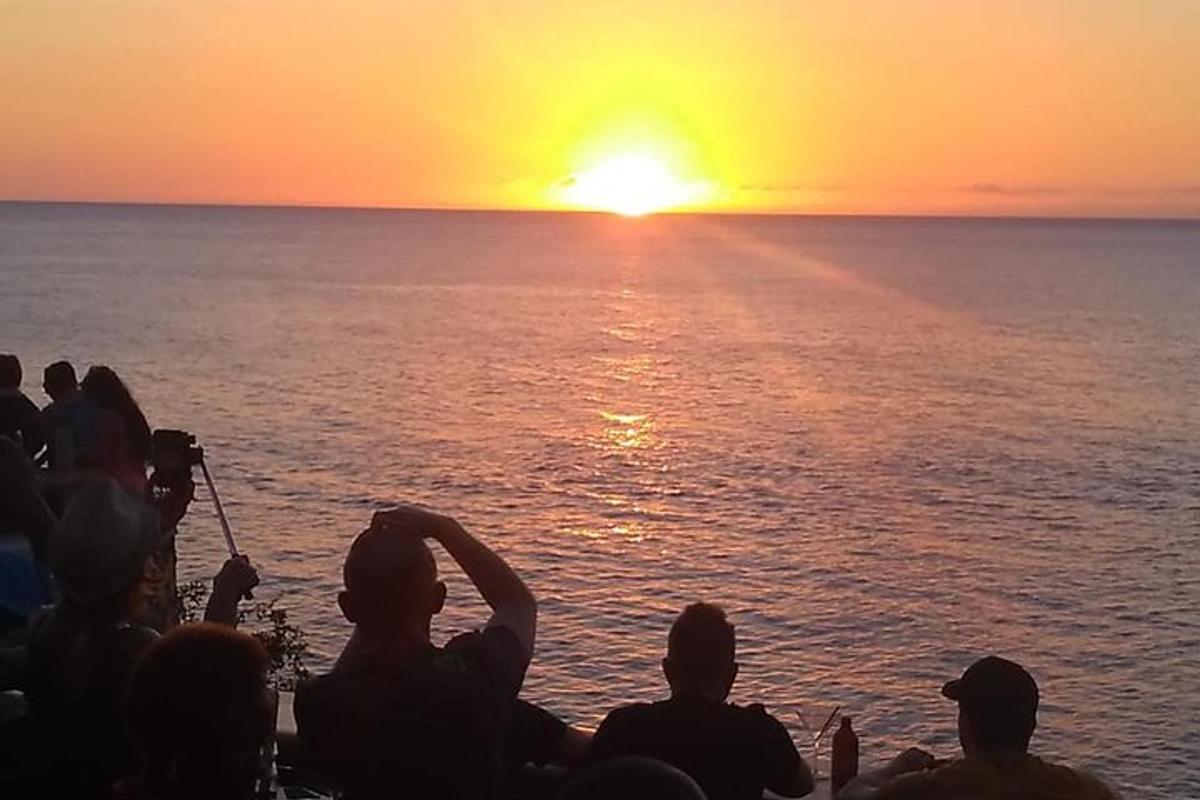 skupina lidí sledujících západ slunce nad oceánem