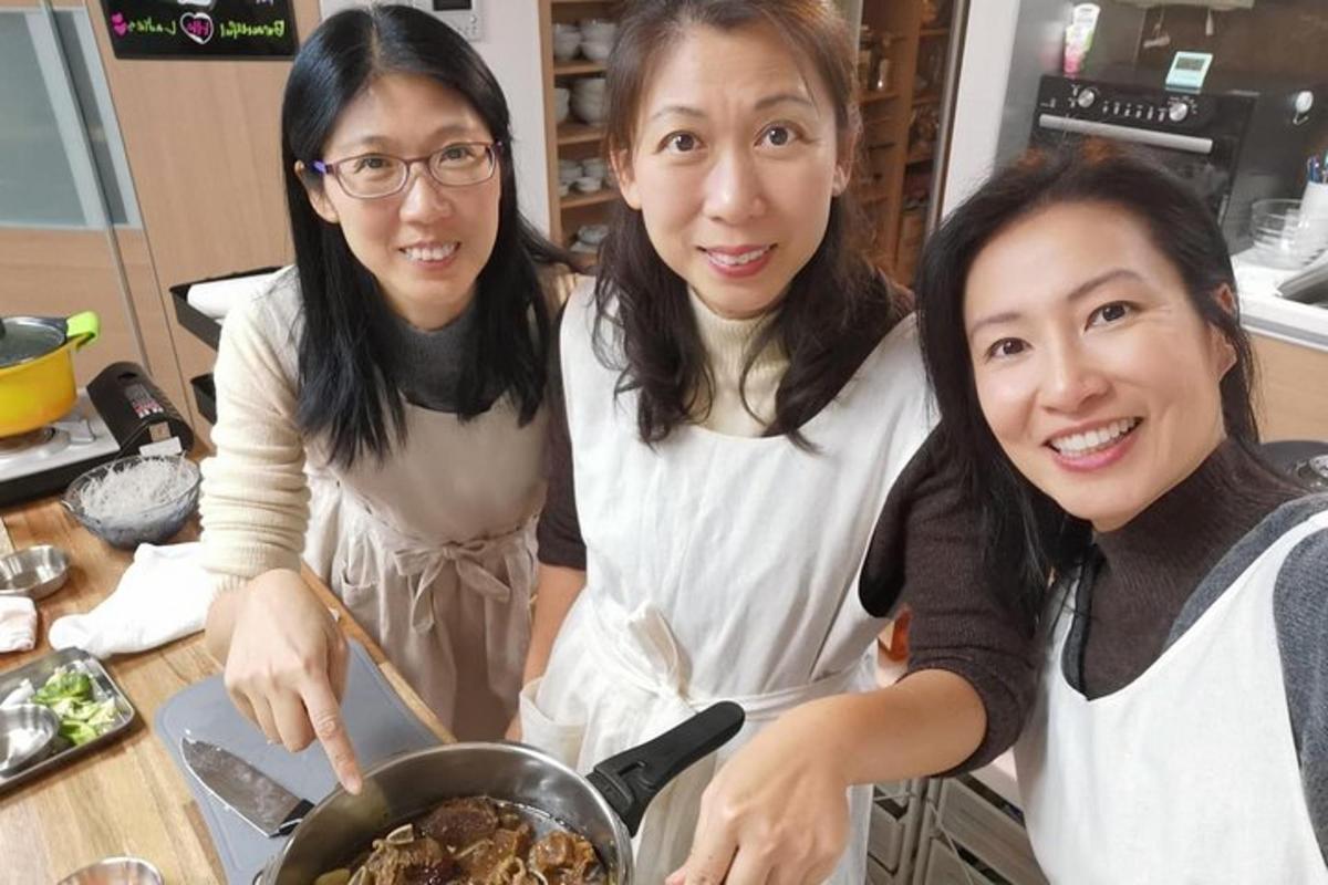 three women standing in a kitchen stirring a pot of food