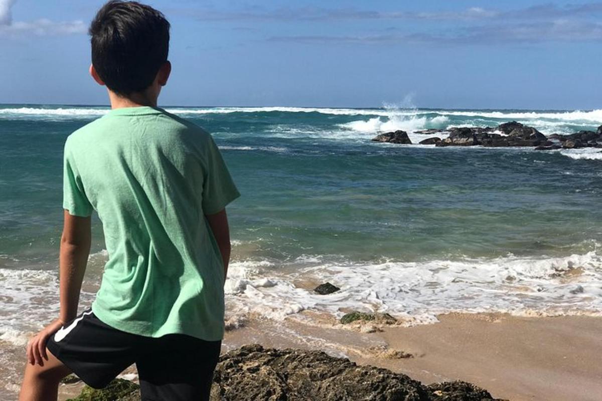 un băiat care stă pe plajă și se uită la ocean