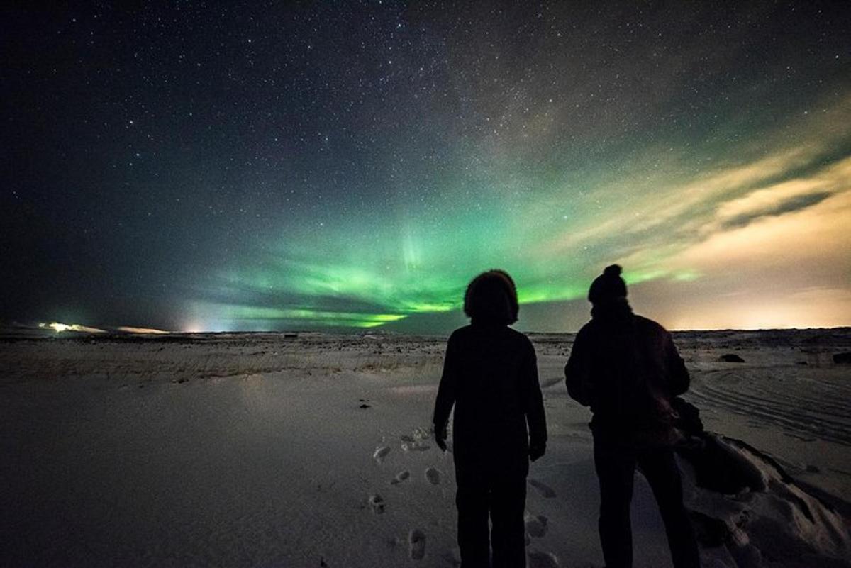 due persone in piedi sulla spiaggia a guardare l'aurora boreale