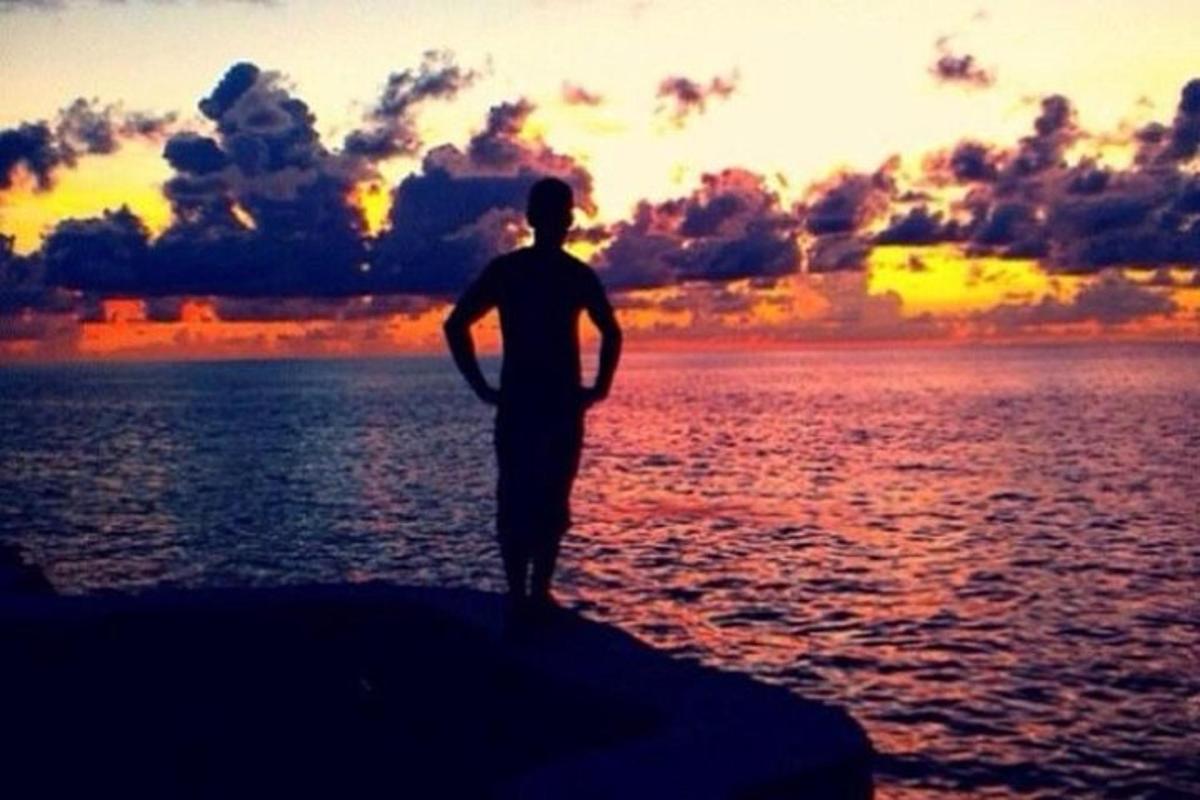 Un hombre parado sobre una roca en el agua al atardecer