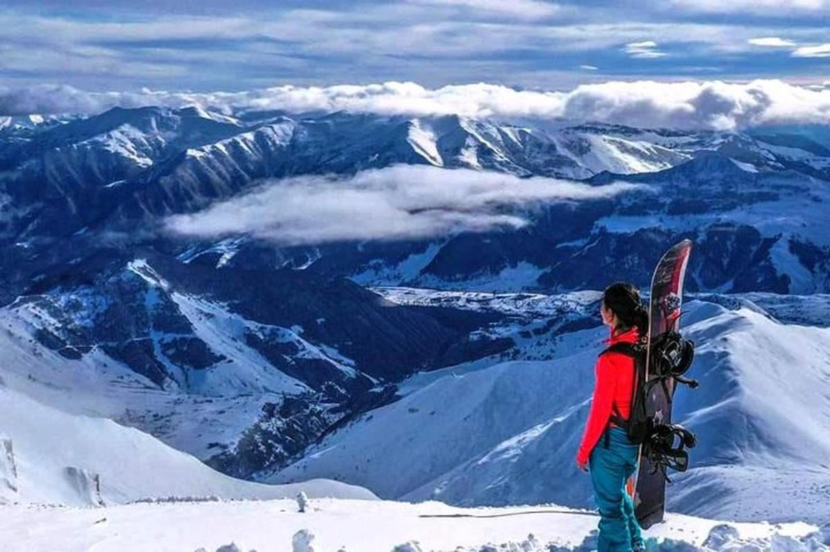 osoba stojící na vrcholu hory se snowboardem