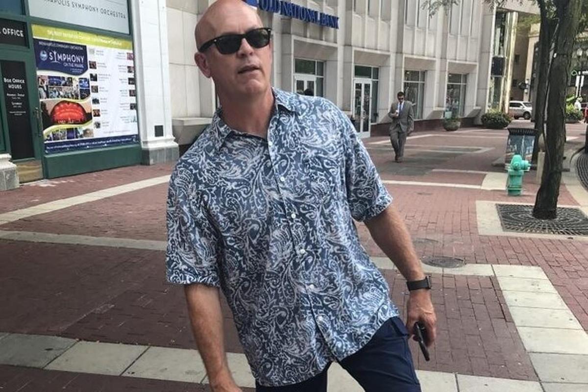 um homem caminhando pela rua de camisa e óculos de sol