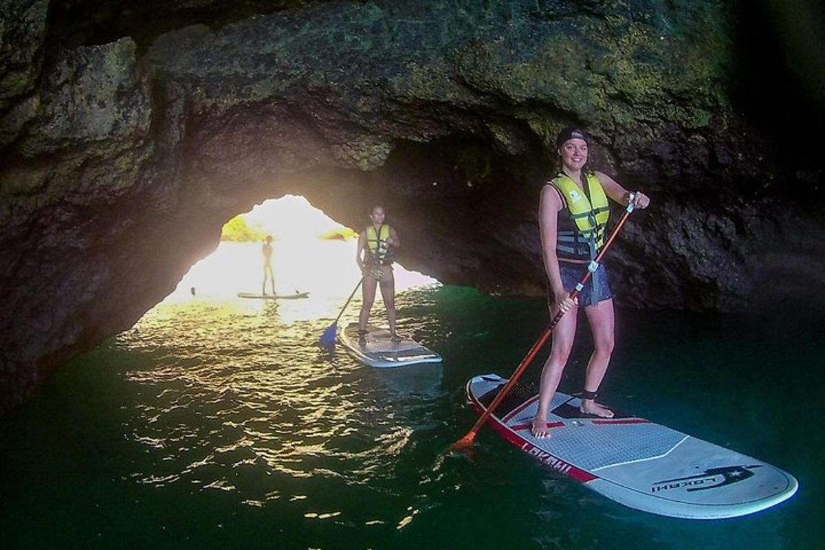 Două persoane stau pe plăci de paddle într-o peșteră