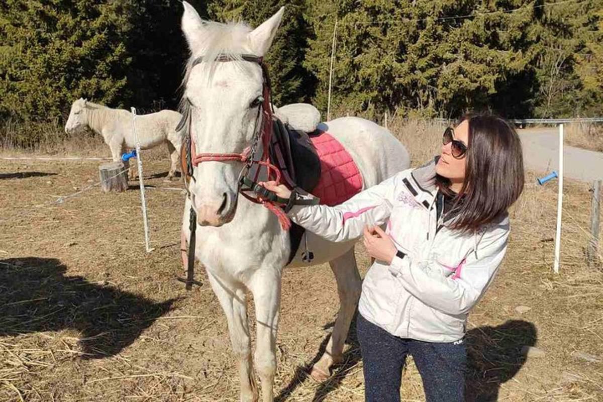 μια γυναίκα που στέκεται δίπλα σε ένα άσπρο άλογο