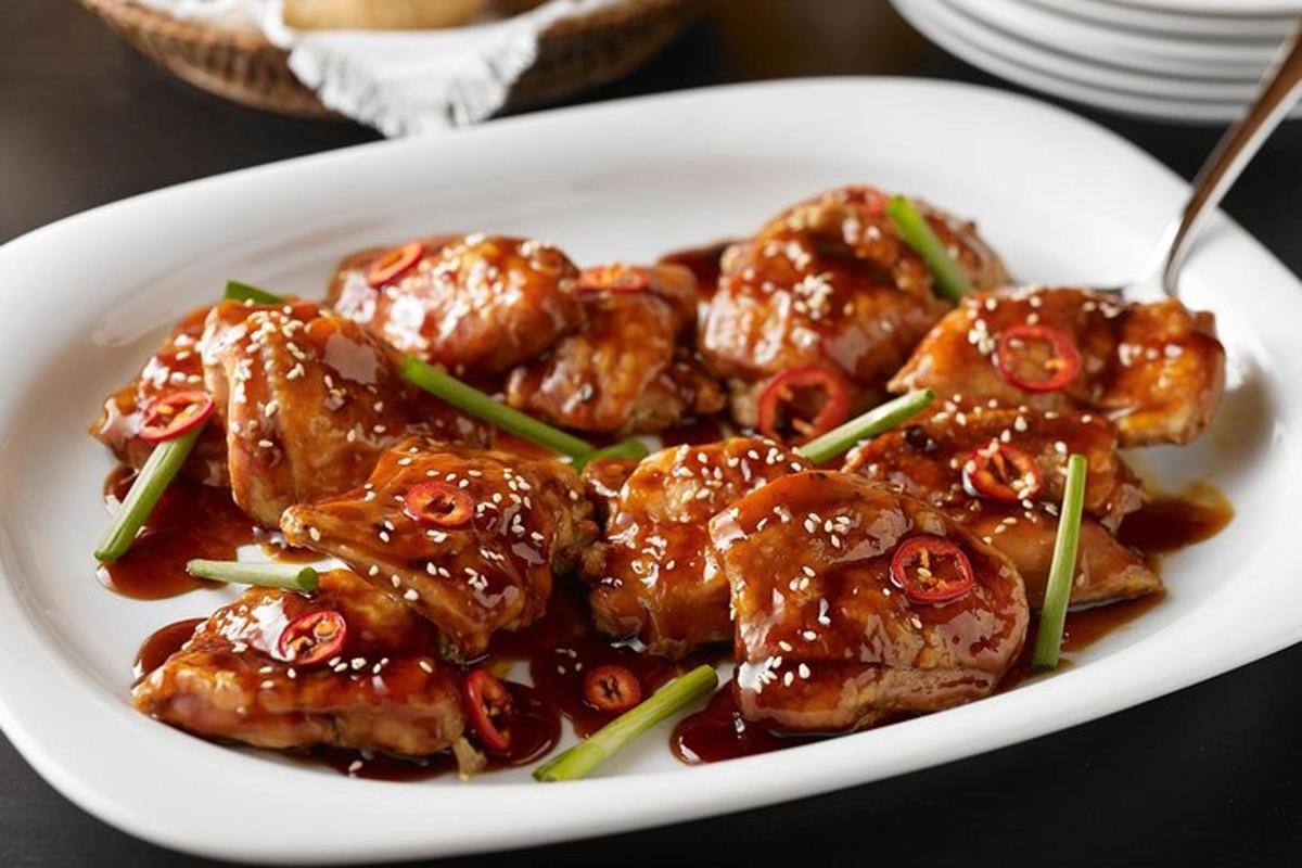 a white plate of food with sesame chicken with sauce