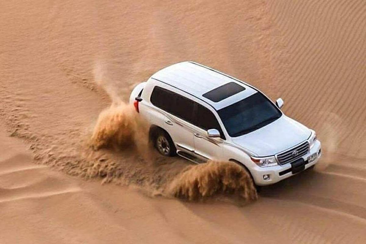 a white truck driving in the sand in the desert