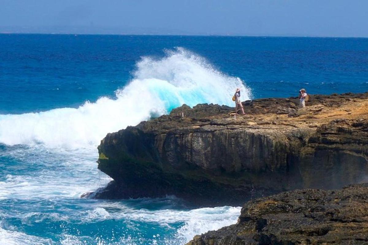 two people standing on a rock in the ocean