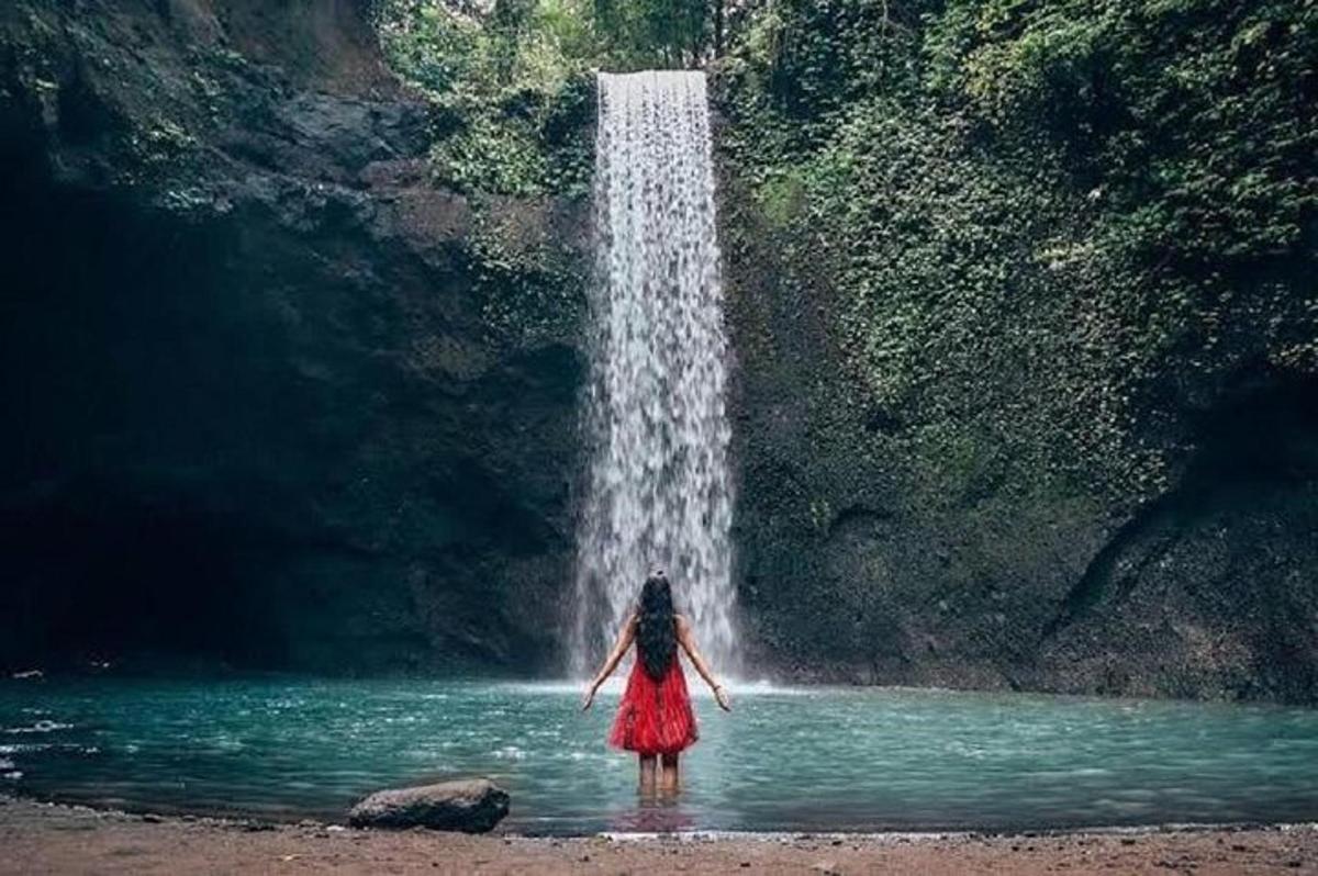 a woman standing in the water in front of a waterfall
