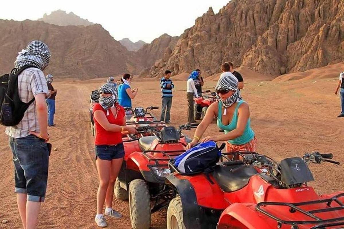 a group of people standing around atvs in the desert