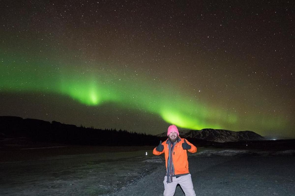 Un hombre está de pie bajo la aurora boreal verde.