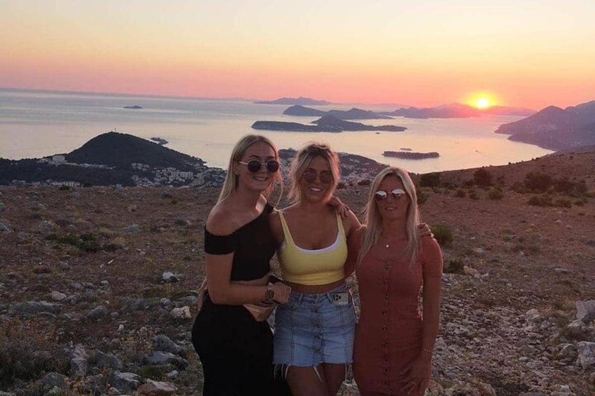 Tre kvinner står på toppen av en ås ved solnedgang