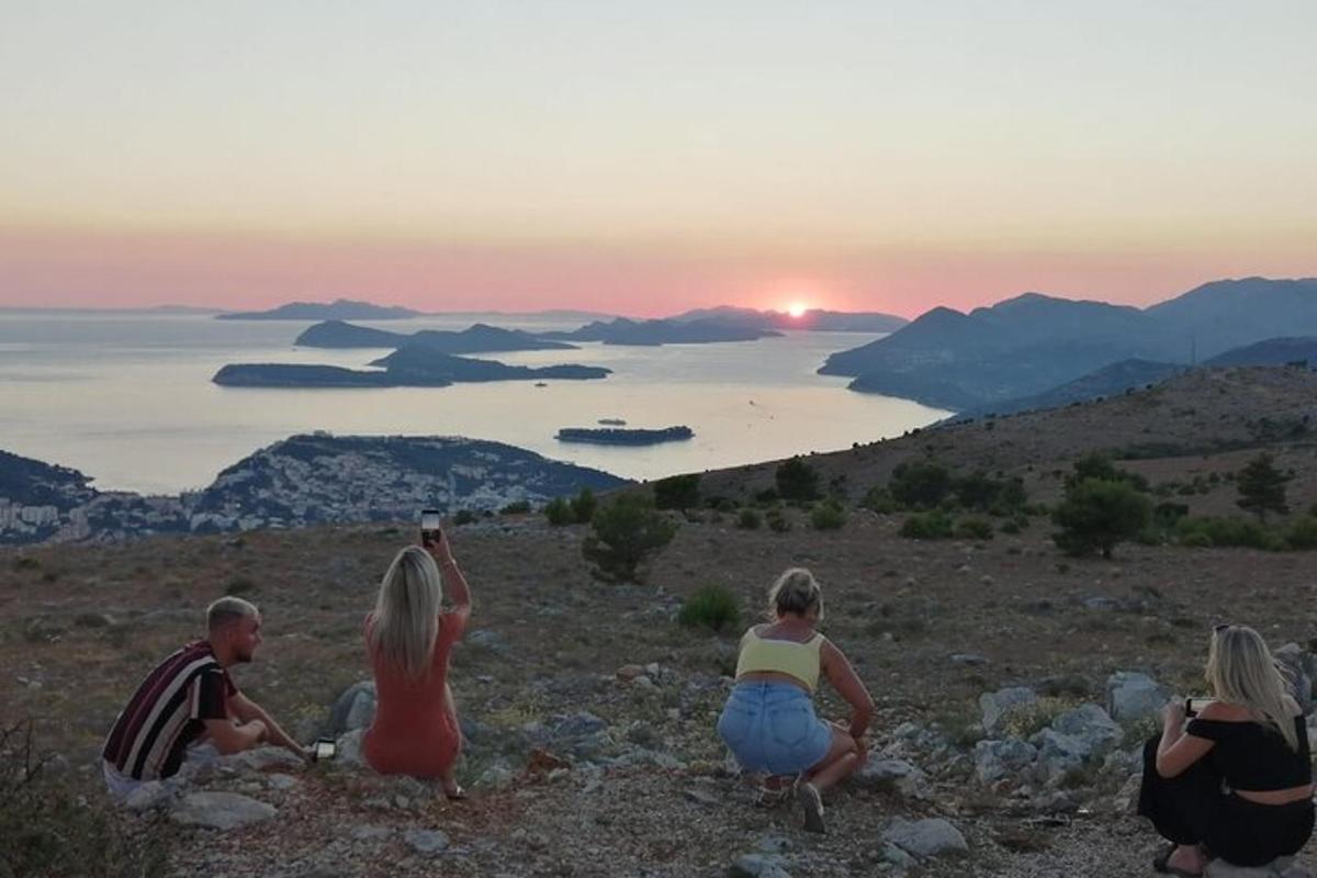 en gruppe mennesker som sitter på en høyde og ser på solnedgangen