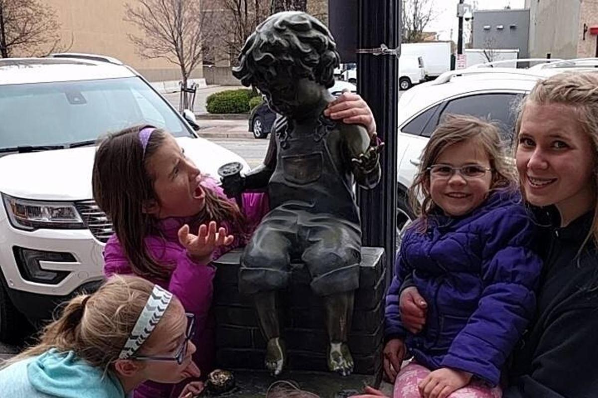 skupina dětí sedících vedle sochy