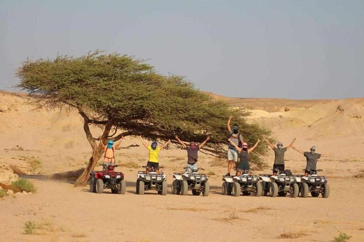 um grupo de pessoas em pé sobre veículos de quatro rodas no deserto