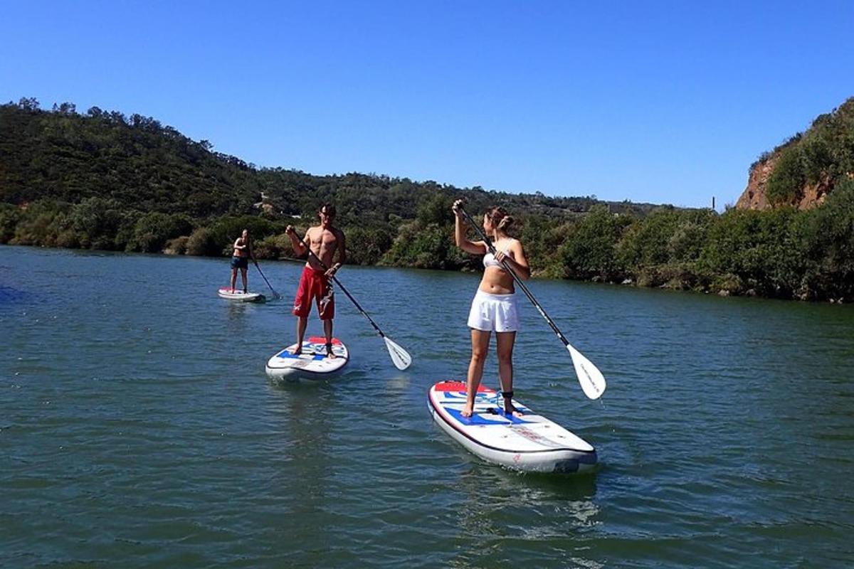 trei persoane fac paddle boarding pe un râu