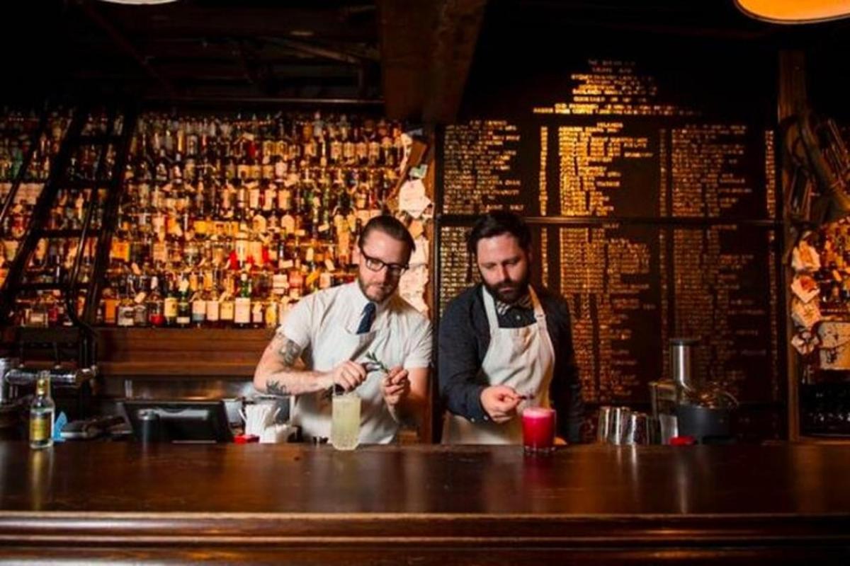 Dos hombres de pie detrás de una barra en un pub.