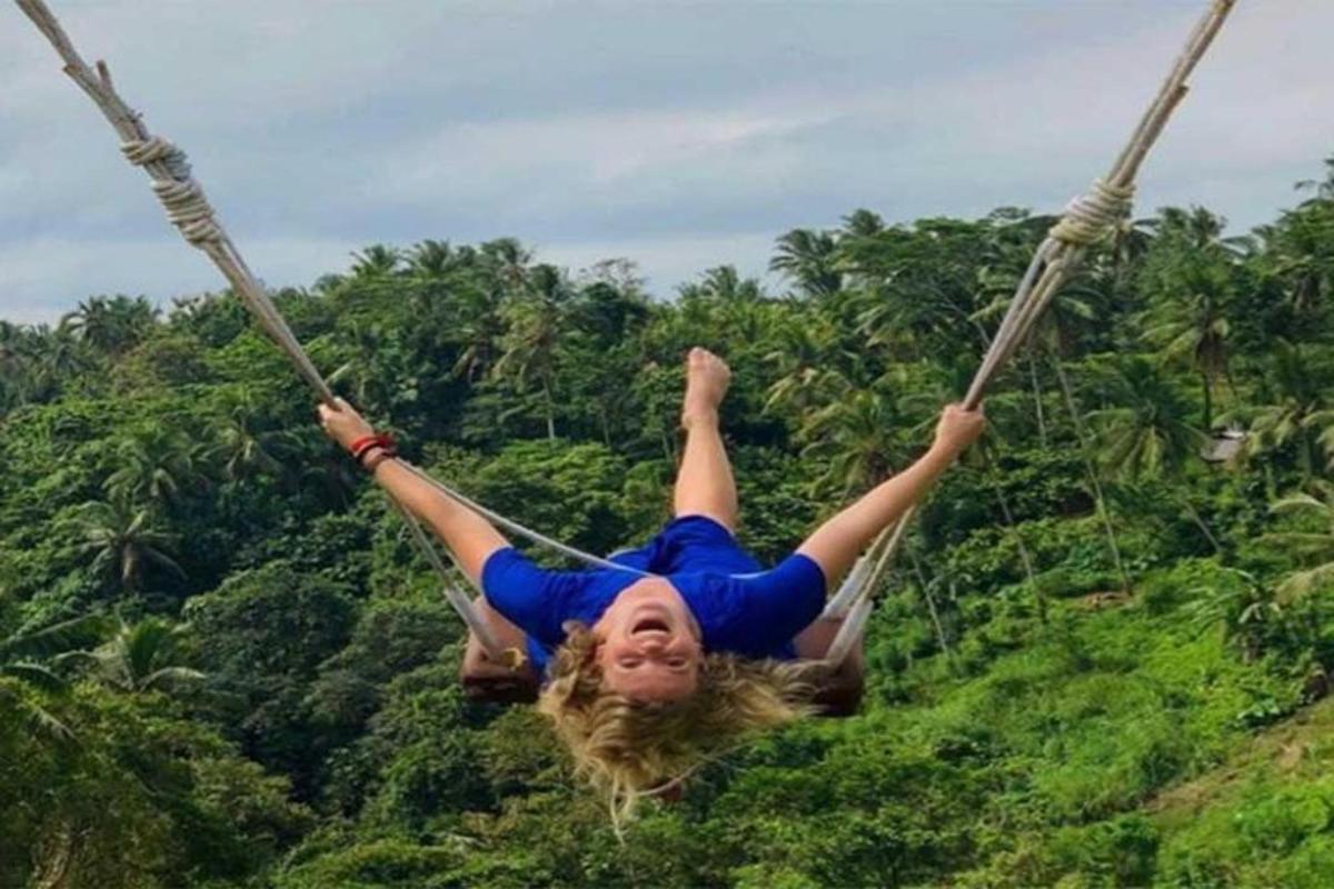 uma mulher balançando em um balanço de corda em frente às árvores