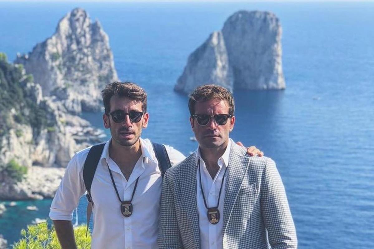 two men standing next to the ocean with mountains in the background