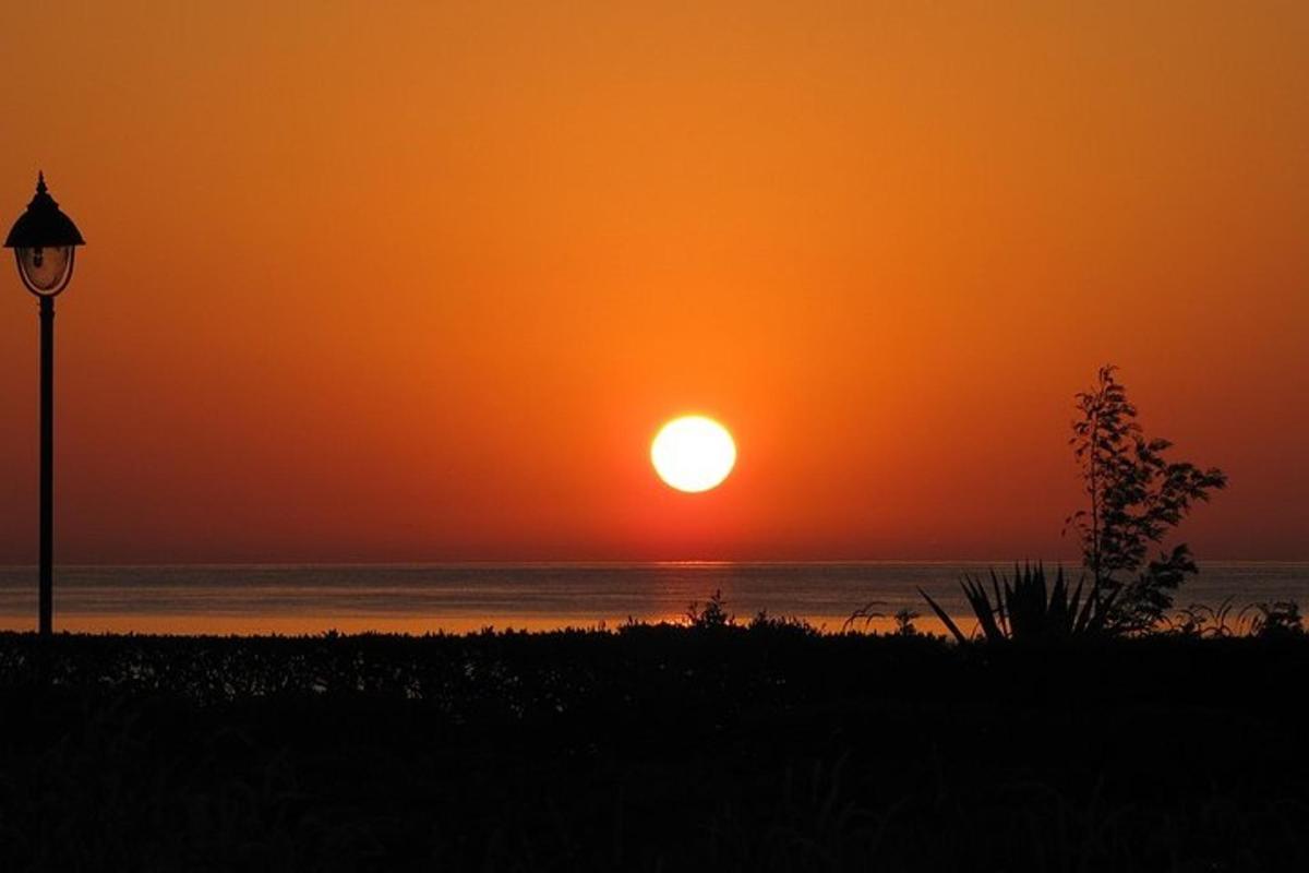 an orange sunset over the ocean with a street light