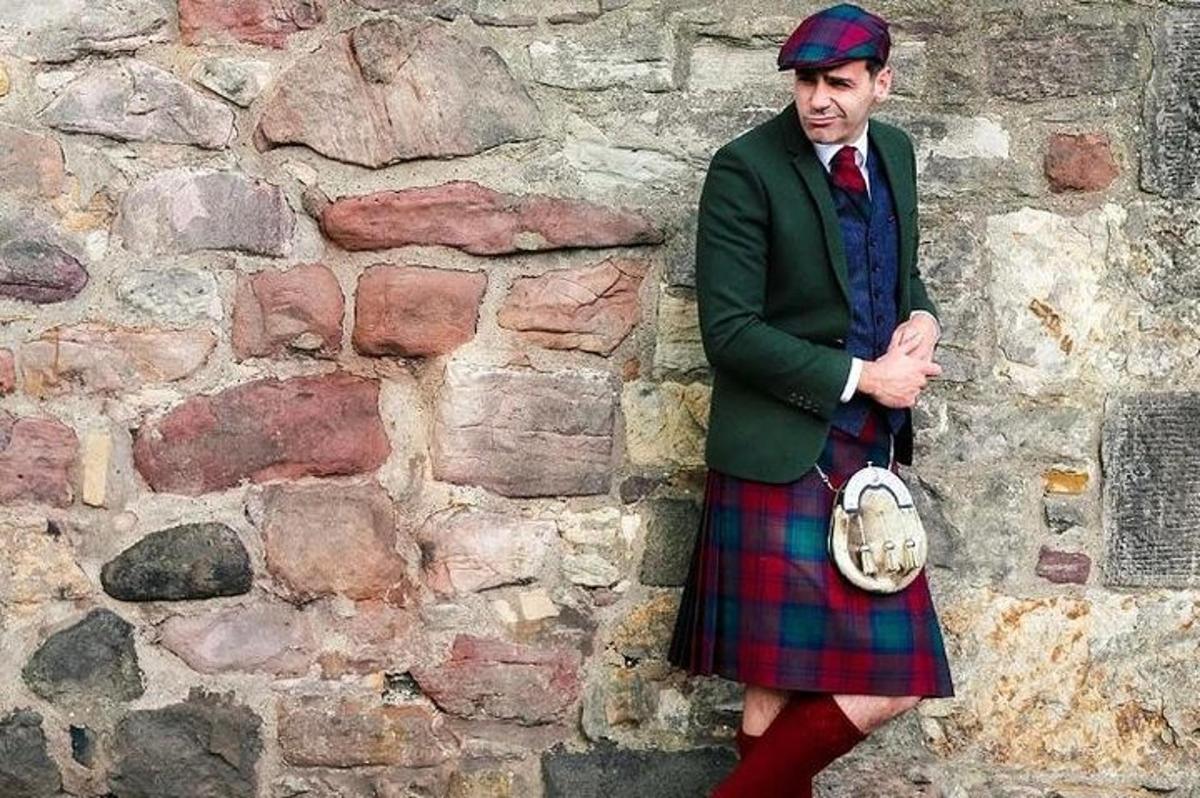 un uomo in kilt in piedi davanti a un muro di pietra
