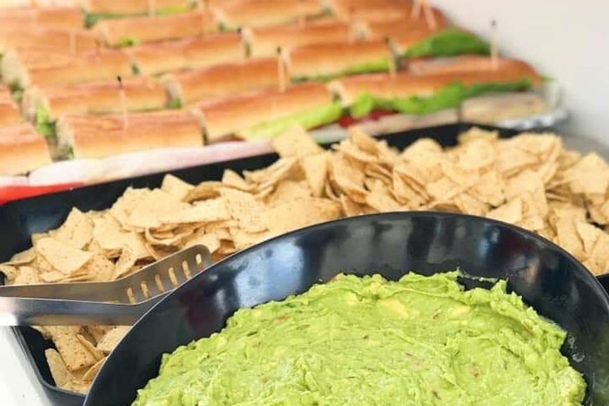 miska guacamole a chipsů vedle talíře sendvičů