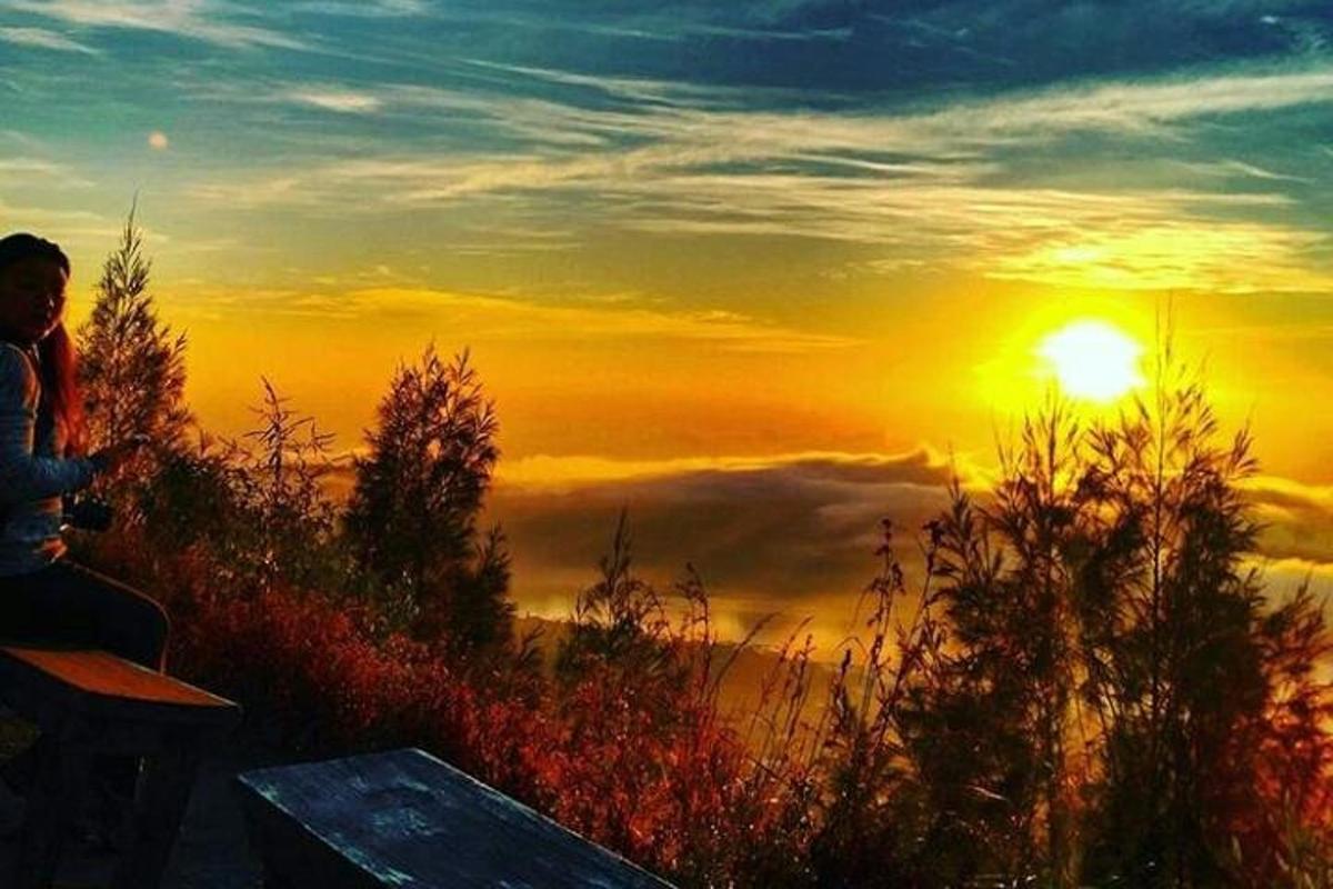 člověk sedící na lavičce a pozorující západ slunce