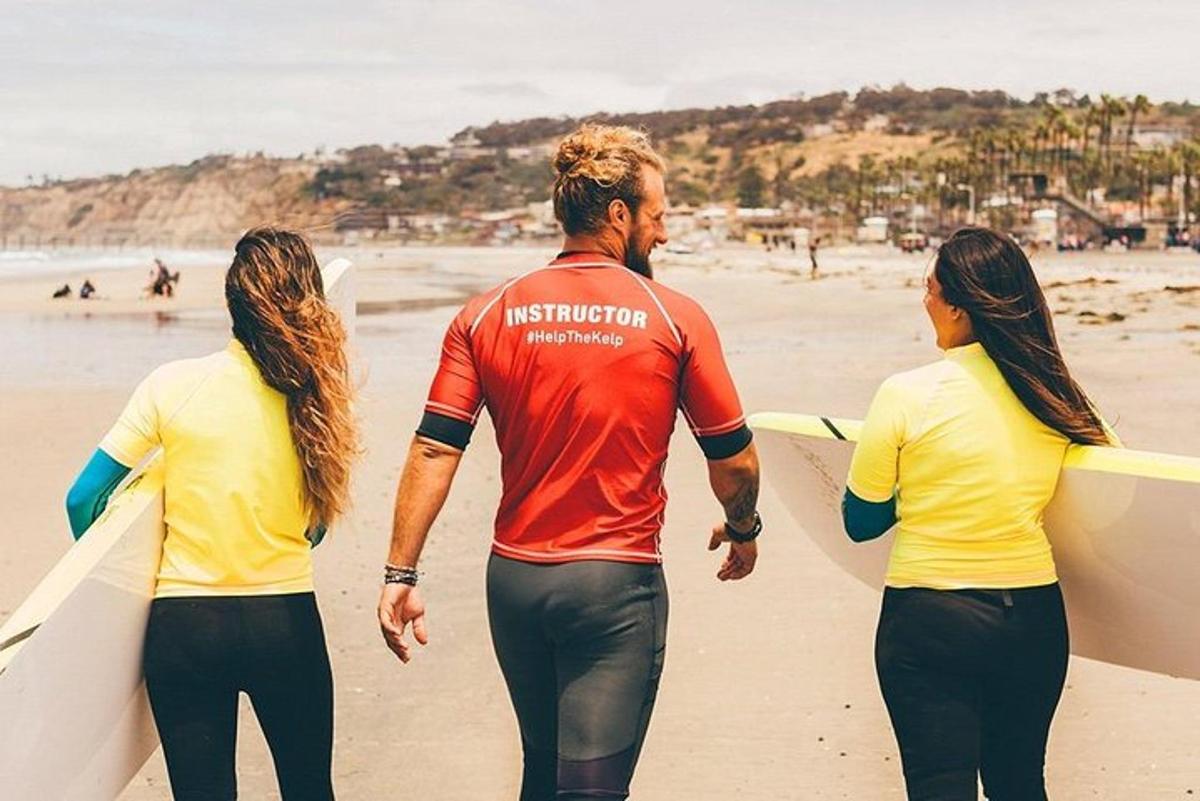 een man en twee vrouwen lopen op het strand met surfplanken