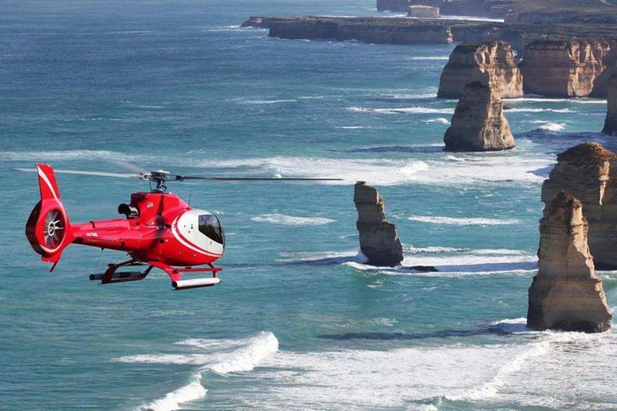 Egy piros helikopter repül az óceán felett, sziklákkal