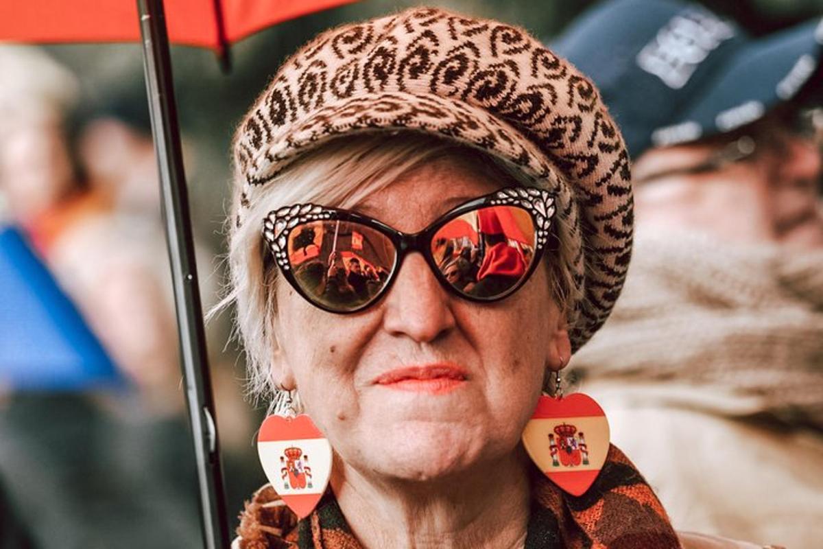 starejša ženska s sončnimi očali in klobukom, ki drži dežnik