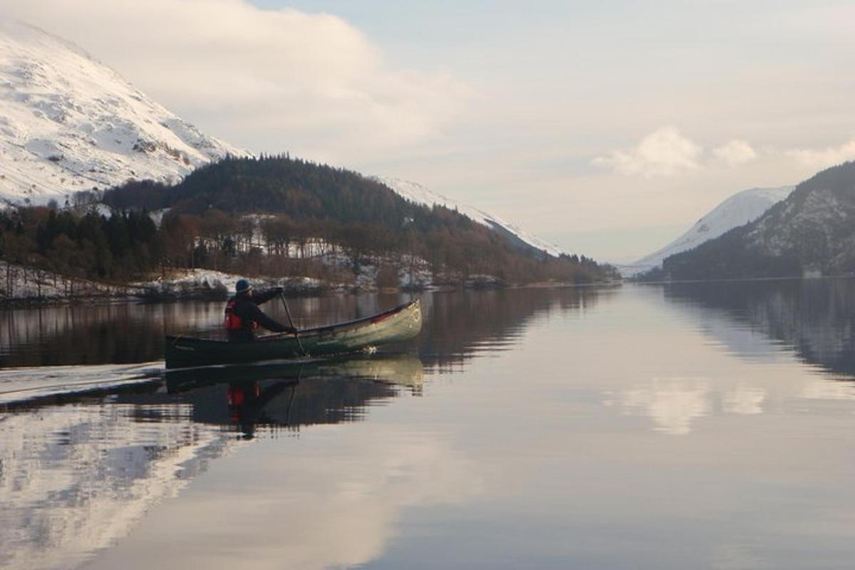 a person in a boat on a lake with snow covered mountains