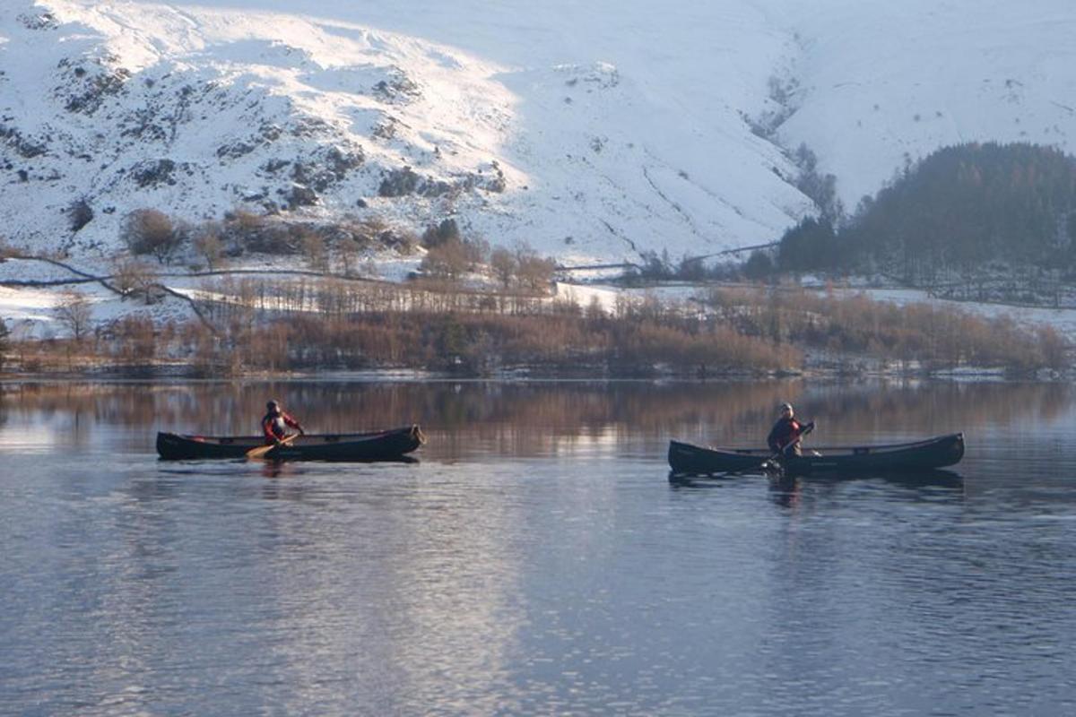 two people in boats on a lake with snow covered mountains