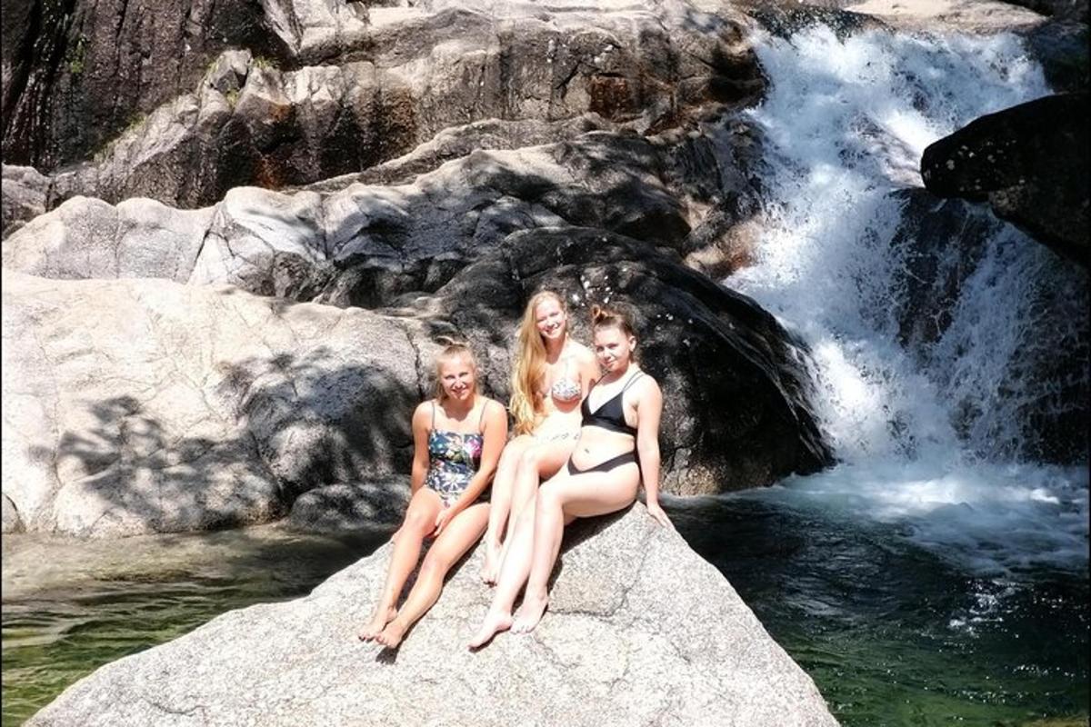 three girls sitting on a rock in front of a waterfall