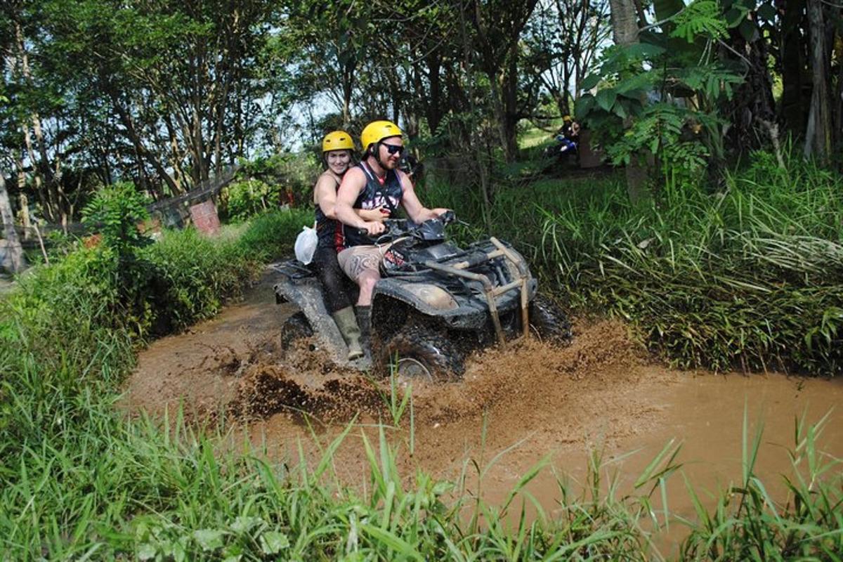 Dos personas viajando en un vehículo de cuatro ruedas por un sendero fangoso.