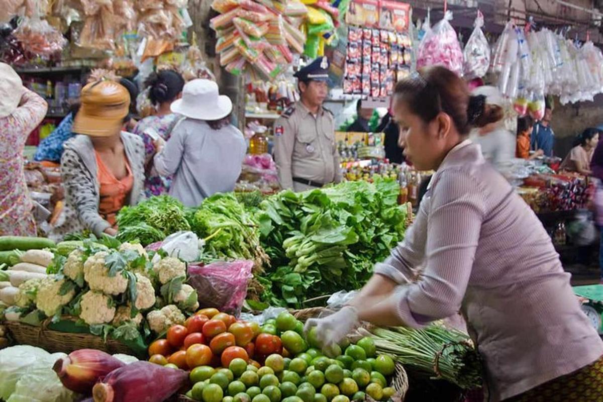 Una mujer parada en un mercado con frutas y verduras.
