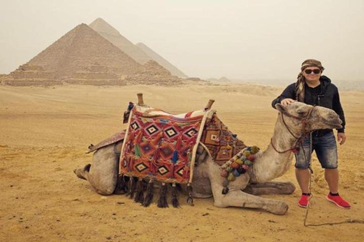 nainen seisoo kamelin vieressä pyramidien edessä