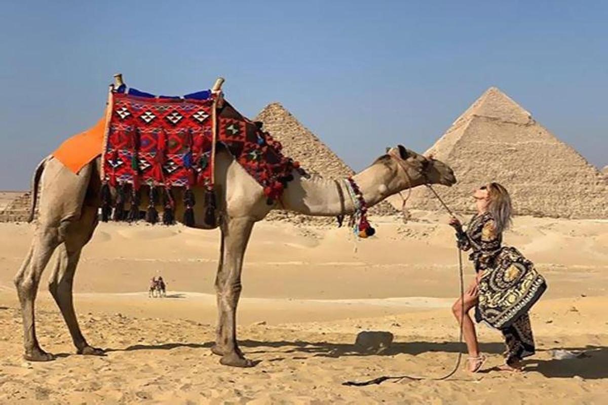 nainen seisoo kamelin vieressä pyramidien edessä