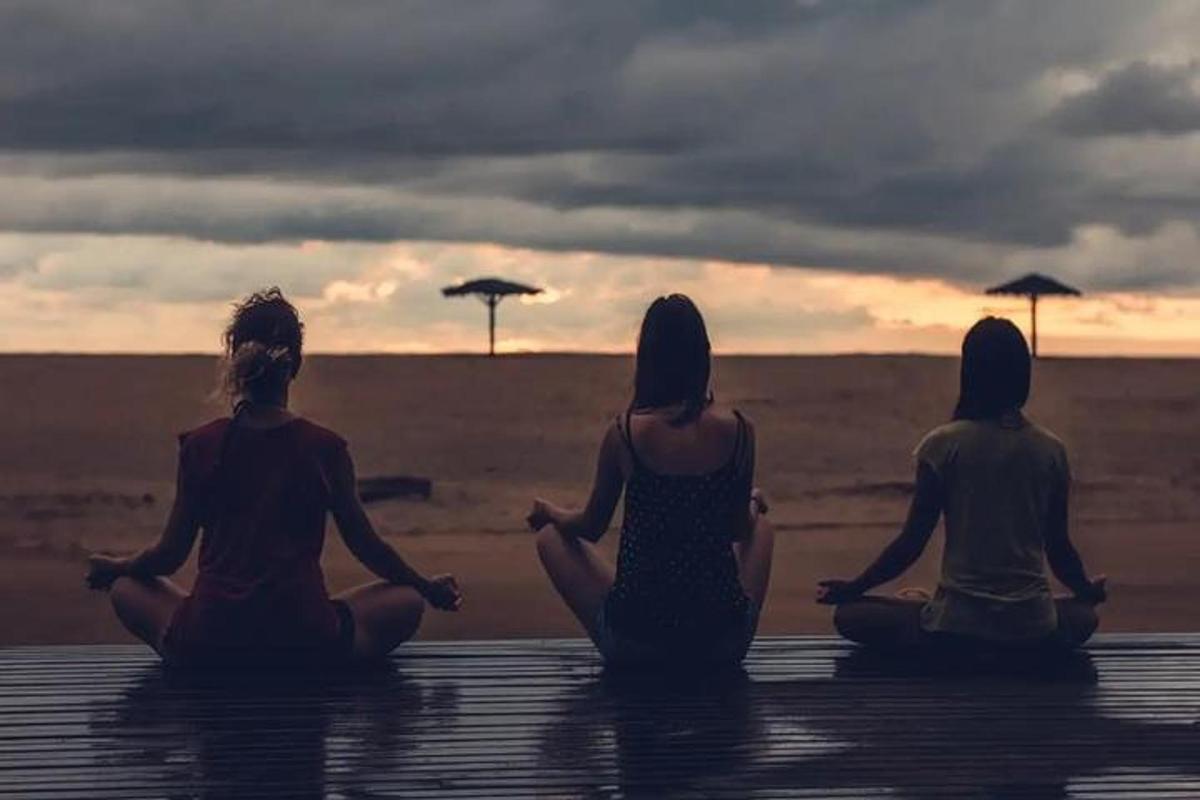 trije ljudje sedijo v meditaciji na plaži