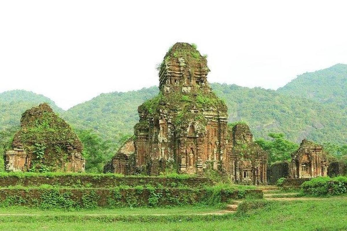 một tòa nhà cũ trên một cánh đồng với những ngọn núi ở phía sau