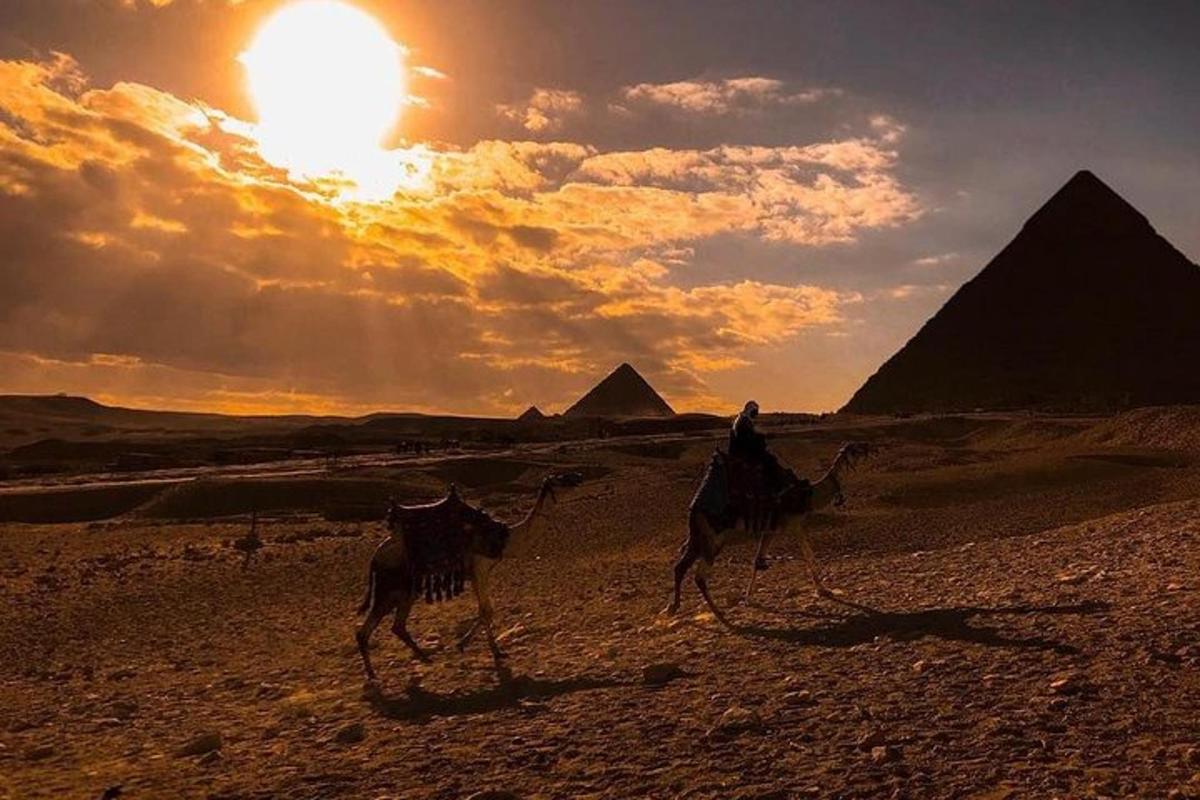 osoba jedoucí na velbloudovi v poušti s pyramidami