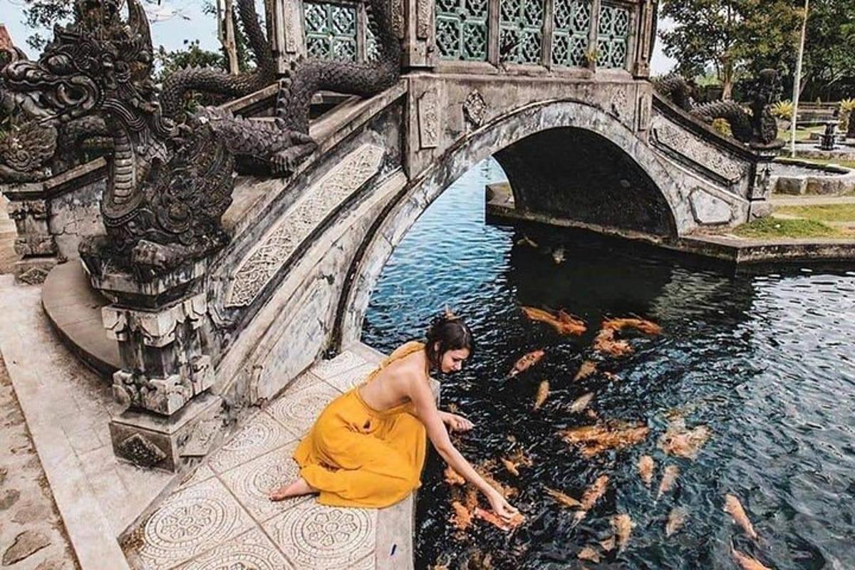 một người phụ nữ mặc áo choàng màu cam đang ngồi dưới nước gần một cây cầu
