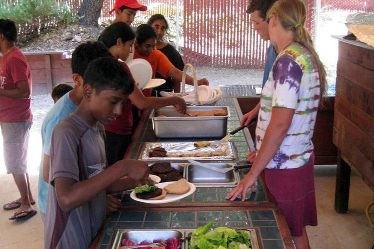 Un grupo de niños de pie alrededor de una mesa con platos de comida.