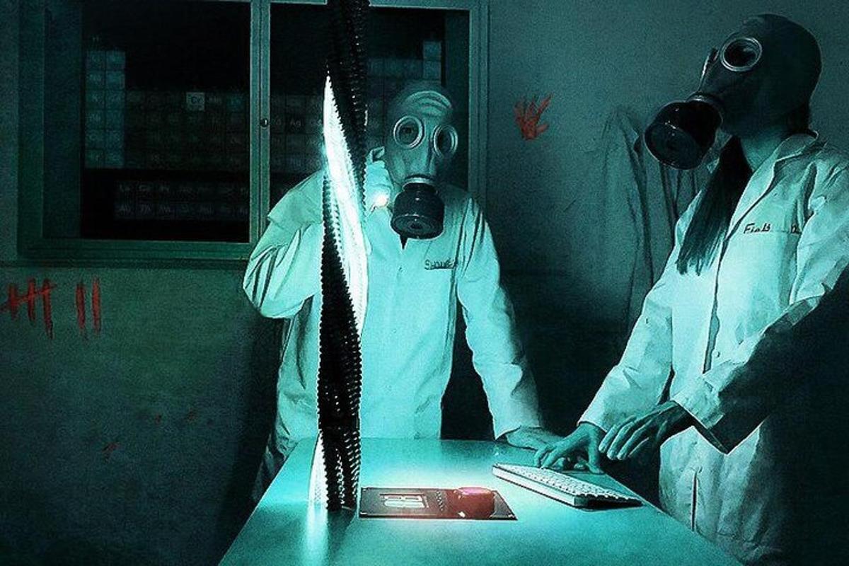 zwei Personen mit Gasmasken stehen an einem Tisch
