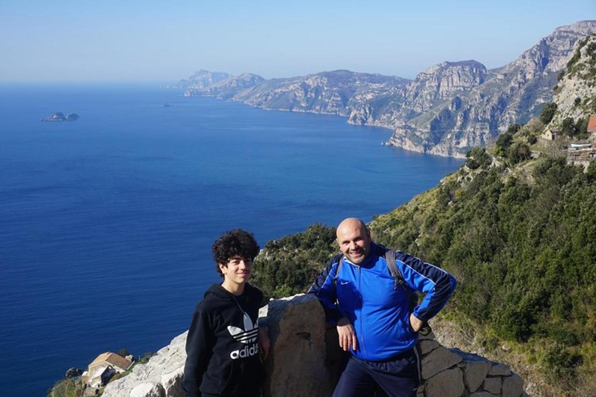 dois homens em pé no topo de uma montanha com vista para o oceano