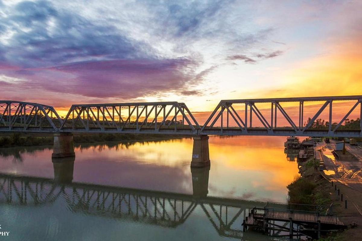 Un puente de tren sobre el agua con una puesta de sol