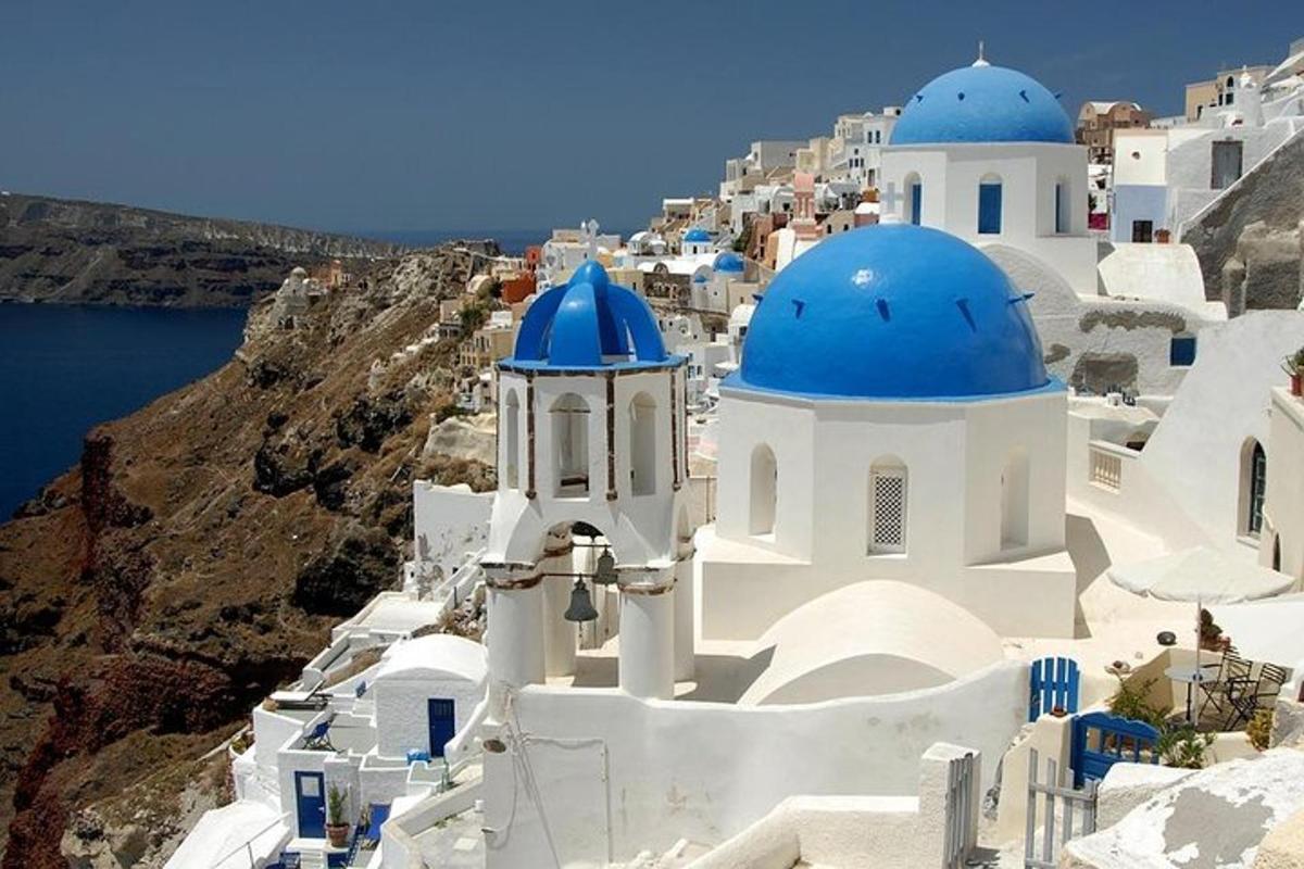 a group of white buildings with blue domes on a cliff